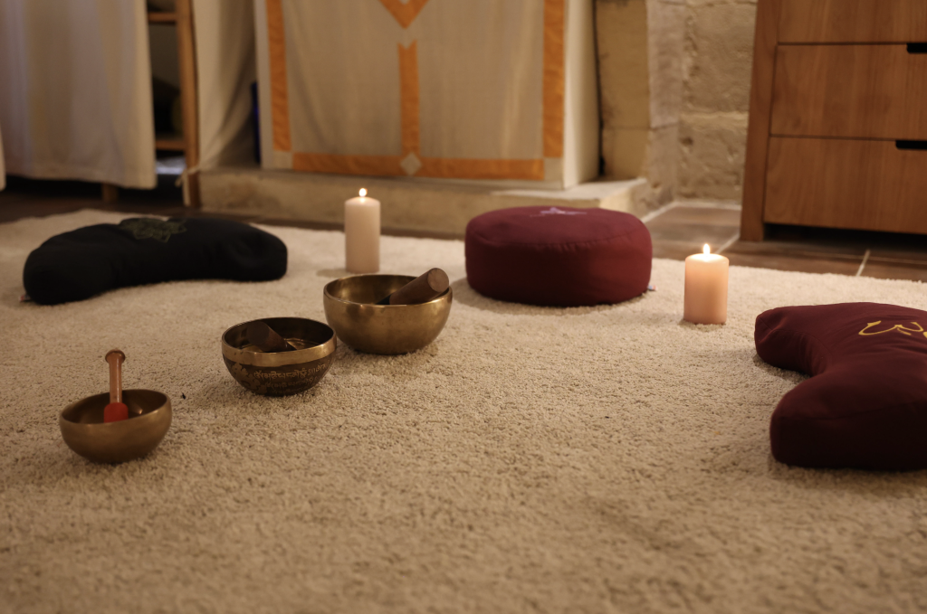 Bols tibétains, coussins de méditation et bougies allumées disposés sur un tapis dans un espace bien-être