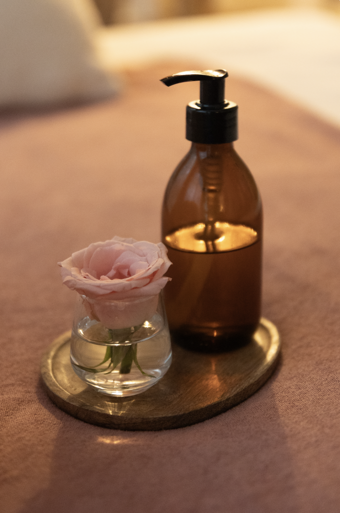 Flacon d’huile de massage et petite rose dans un vase posés sur un plateau en bois