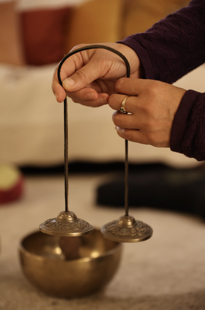 Mains tenant une paire de cymbales tibétaines au-dessus d’un bol chantant dans un espace bien-être
